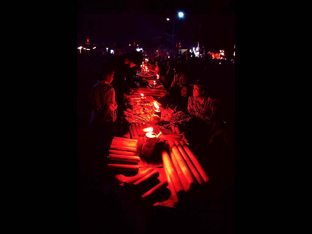 祭の夜 仏塔前には多くの露天が並び アセチレンの炎に人びとの顔が赤く浮かぶ　焼き鳥や甘いもち米 蒸かした生まれかけのアヒルの卵などが売られている　タット・ルアン大祭　ビエンチャン